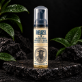 Reuzel Wood and Spice Beard Foam 70 ml on dark stone with green leaves