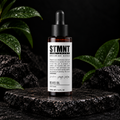 STMNT Grooming Goods Beard Oil 50 ml on dark stone with green leaves